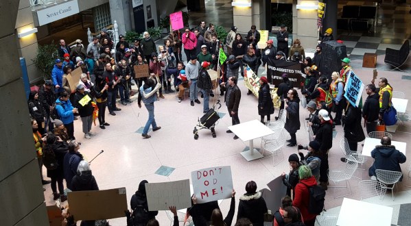 A crowd of people gathered in a circle inside a government building with speakers and signs