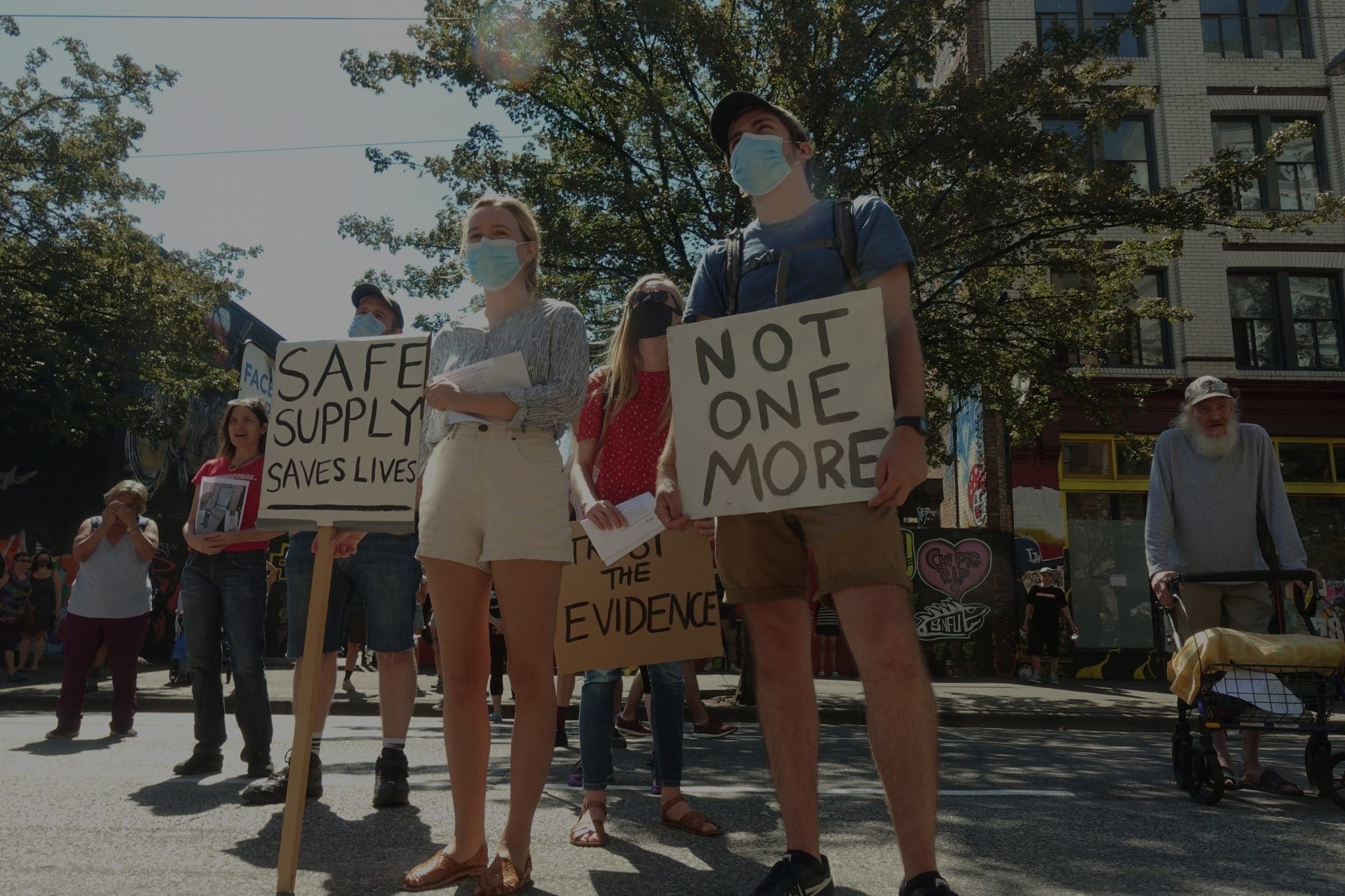 three people holding up signs at the safe supply rally in Vancouver, 2020