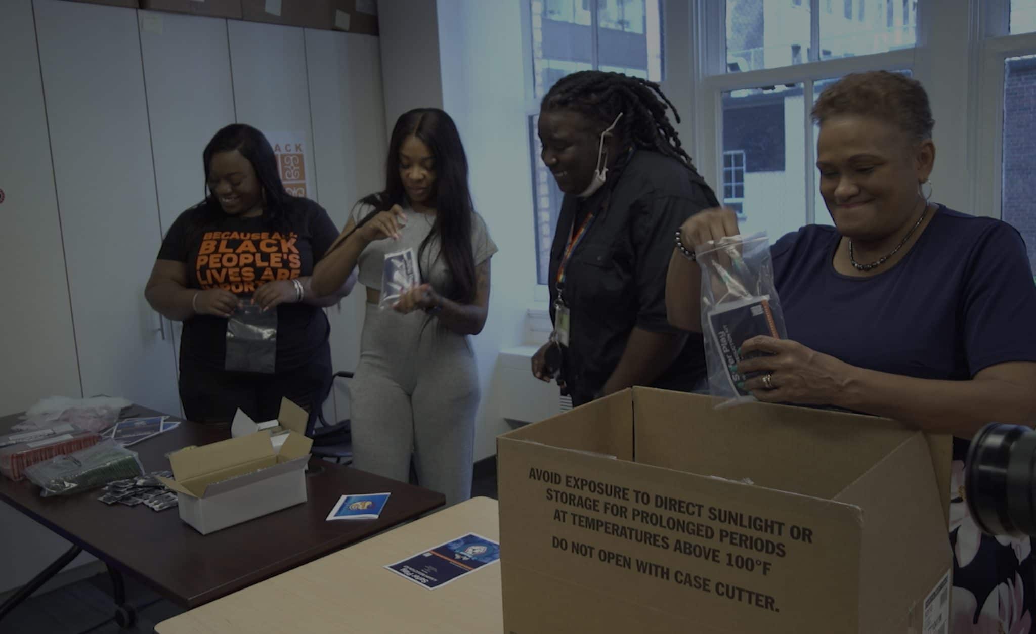Four Black women stuffing harm reduction packages